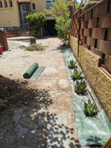 Allée pavée en cours d'aménagement. Rouleau de toile de paillage et succulentes alignées le long d'un mur décoratif rouillé.